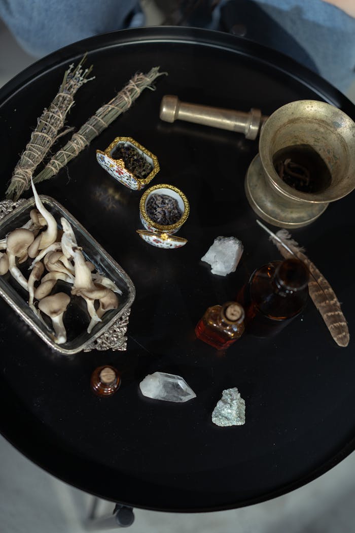 Enchanting flat lay featuring mystical objects like crystals, dried herbs, and glass bottles on a black round table.